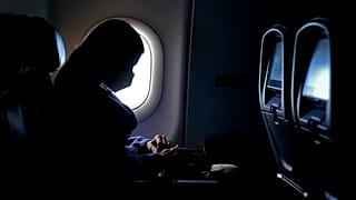 سيدة ترتدي كمامة وتجلس داخل طائرة
