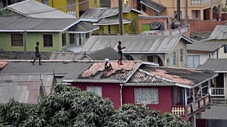 Varias personas limpian la ceniza volcánica del tejado de una casa tras la erupción del volcán La Soufriere, en San Vicente