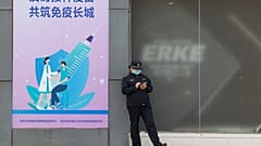 A worker stands outside a vaccination site with a sign saying "Timely vaccination to build the Great Wall of Immunity together" in Beijing. April 9, 2021.