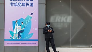 A worker stands outside a vaccination site with a sign saying "Timely vaccination to build the Great Wall of Immunity together" in Beijing. April 9, 2021.