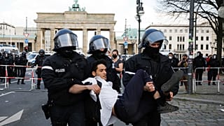 Police officers carry away a demonstrator after police stop a protest rally near the Brandenburg Gate