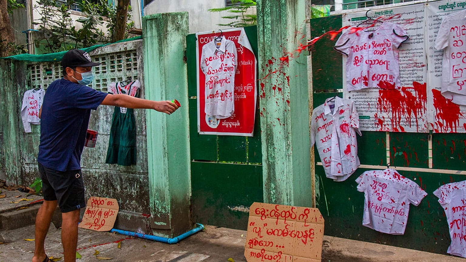 An anti-coup protester splashes red paint on student uniforms after they hanged them outside a school during a demonstration against the re-opening of the school by the junta 