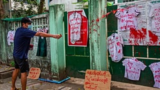 An anti-coup protester splashes red paint on student uniforms after they hanged them outside a school during a demonstration against the re-opening of the school by the junta 
