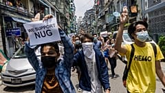 A protester holds a sign in support of the National Unity Government (NUG) as others make the three-finger salute during a demonstration against the military coup