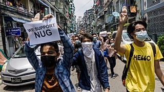A protester holds a sign in support of the National Unity Government (NUG) as others make the three-finger salute during a demonstration against the military coup