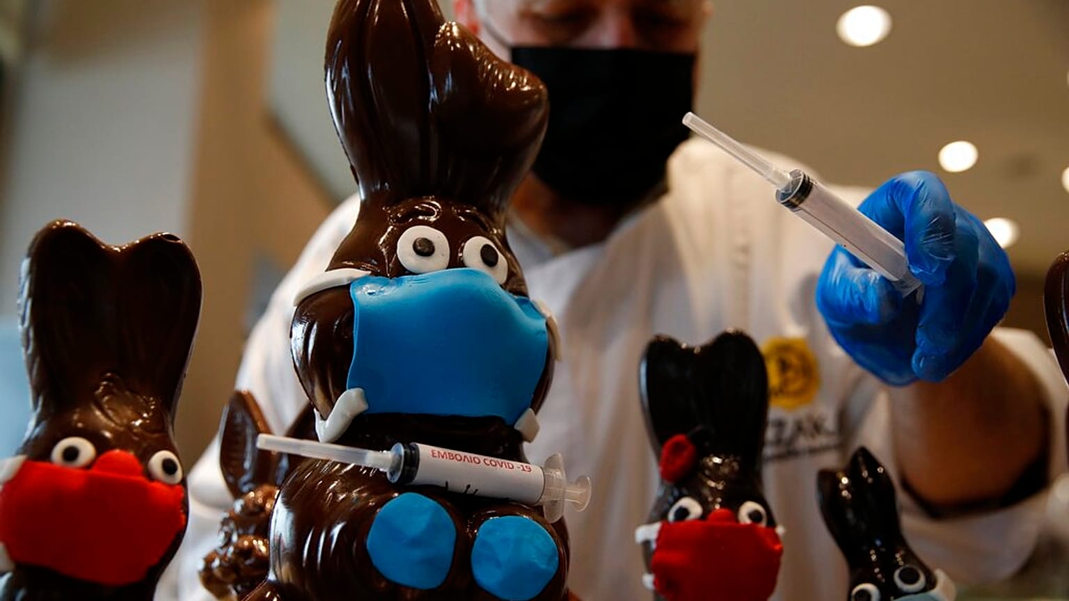 Tassos Vazakas, owner of a cake shop, prepares chocolate bunnies with masks and a vaccination syringe during Holy Week in Athens,
