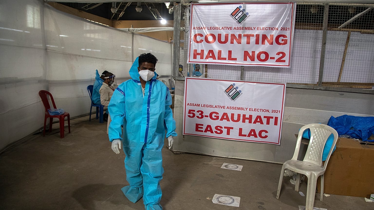 A counting agent in protective suit walks past officials during the counting of votes of Assam state assembly election in Gauhati, India, Sunday, May 2, 2021. 