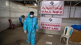 A counting agent in protective suit walks past officials during the counting of votes of Assam state assembly election in Gauhati, India, Sunday, May 2, 2021. 