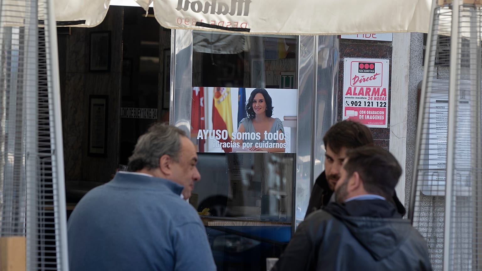 People sit outside a bar with a poster of the president of the Madrid autonomous government, Isabel Diaz Ayuso, on March 22, 2021.