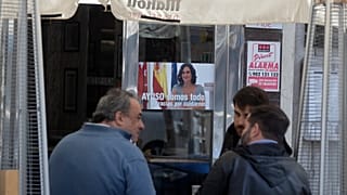 People sit outside a bar with a poster of the president of the Madrid autonomous government, Isabel Diaz Ayuso, on March 22, 2021.