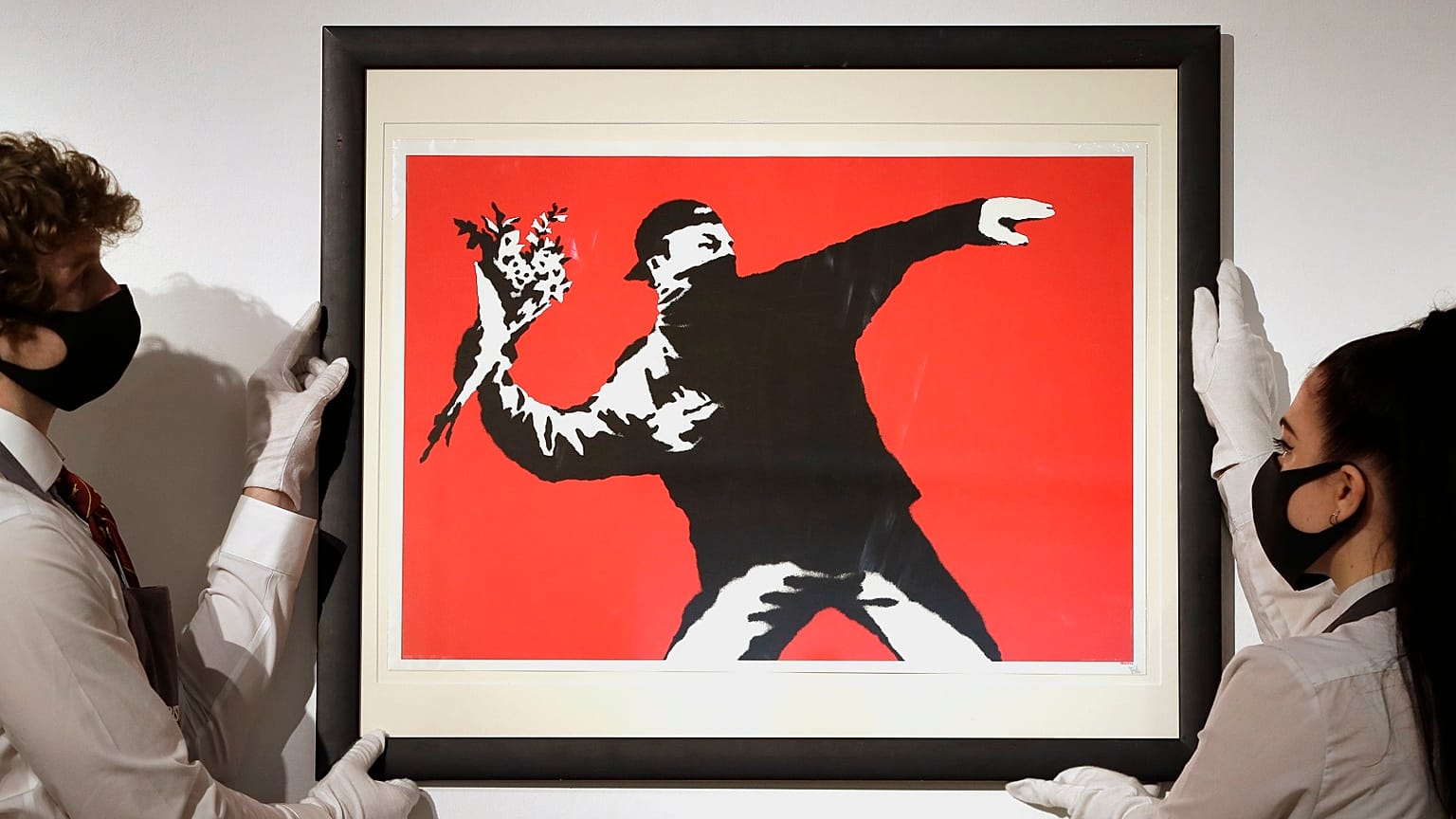 Gallery technicians display a Banksy artwork called "Love is in the Air" read for auction.