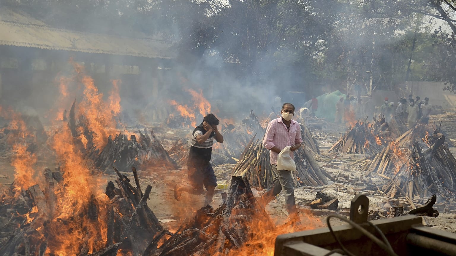 In this April 29, 2021, file photo, relatives react to heat emitting from the multiple funeral pyres of COVID-19 victims at a crematorium in the outskirts of New Delhi, India.
