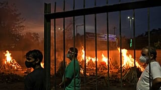 People watch burning funeral pyres of their relatives who died of COVID-19 in a ground that has been converted into a crematorium in New Delhi, India, Thursday, May 6, 2021.
