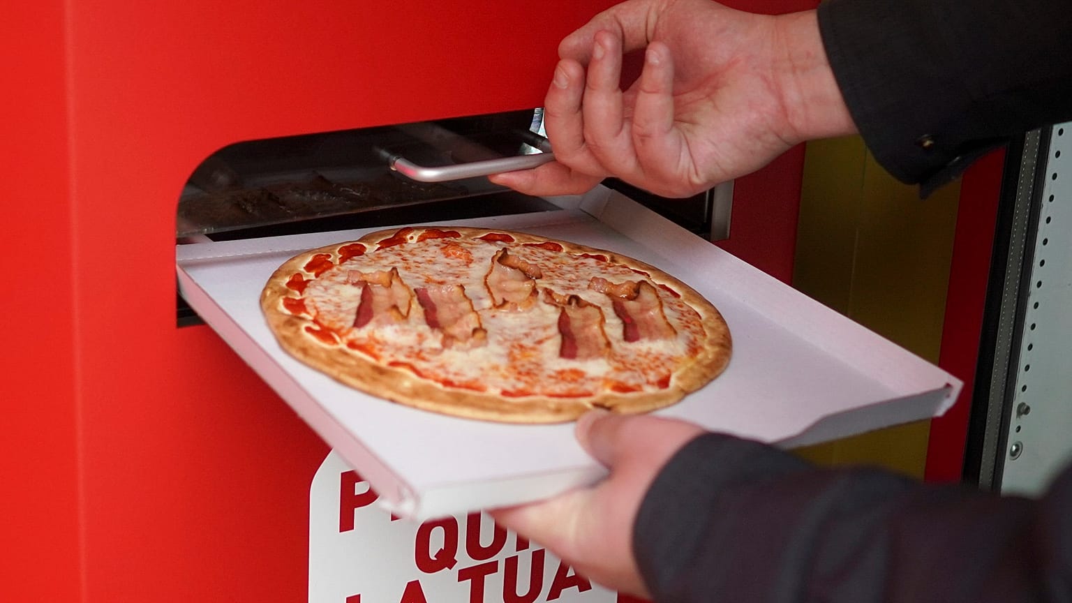 Elkészült pizzát vesz ki egy férfi az automatából