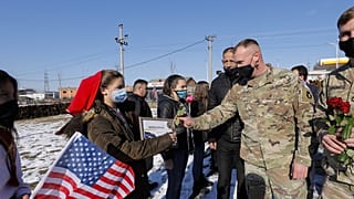 Koszovói albán nők virágot nyújtanak át amerikai békefenntartóknak, januárban