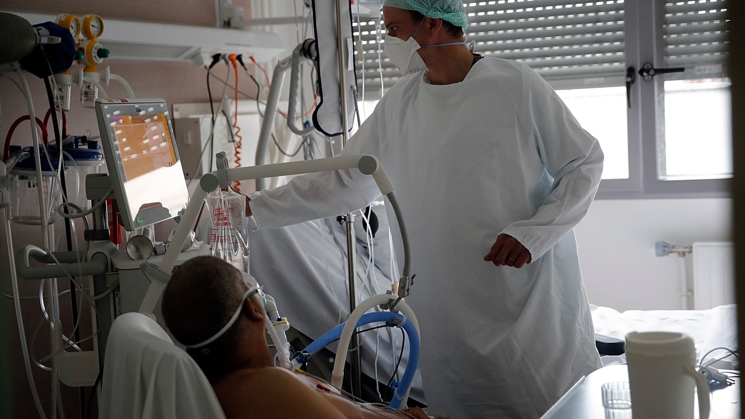 أحد أعضاء الطاقم الطبي يعتني بمريض مصاب بفيروس كورونا في وحدة العناية المركزة في مستشفى شارل نيكول العام في روان - فرنسا