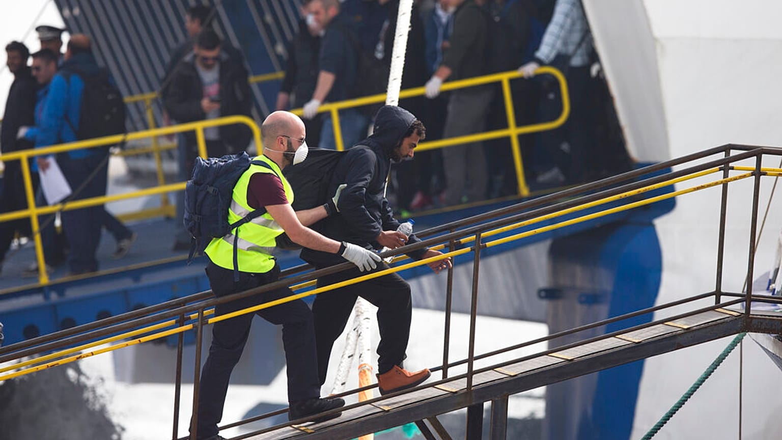 Un agente de la agencia de protección de fronteras de la Unión Europea, Frontex, conduce a un migrante para que embarque en un transbordador en Grecia en 2016