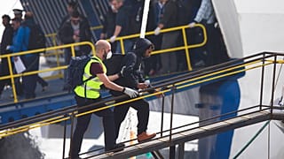 Un agente de la agencia de protección de fronteras de la Unión Europea, Frontex, conduce a un migrante para que embarque en un transbordador en Grecia en 2016