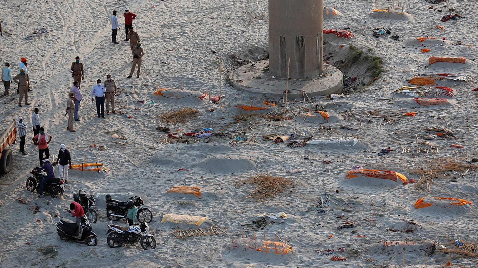 Policemen stand next to the bodies buried in shallow graves on the banks of Ganges river in Prayagraj, India, Saturday, May 15, 2021. 