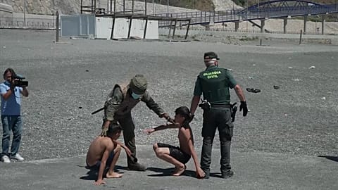 Boys sitting down on beach with soldiers around them