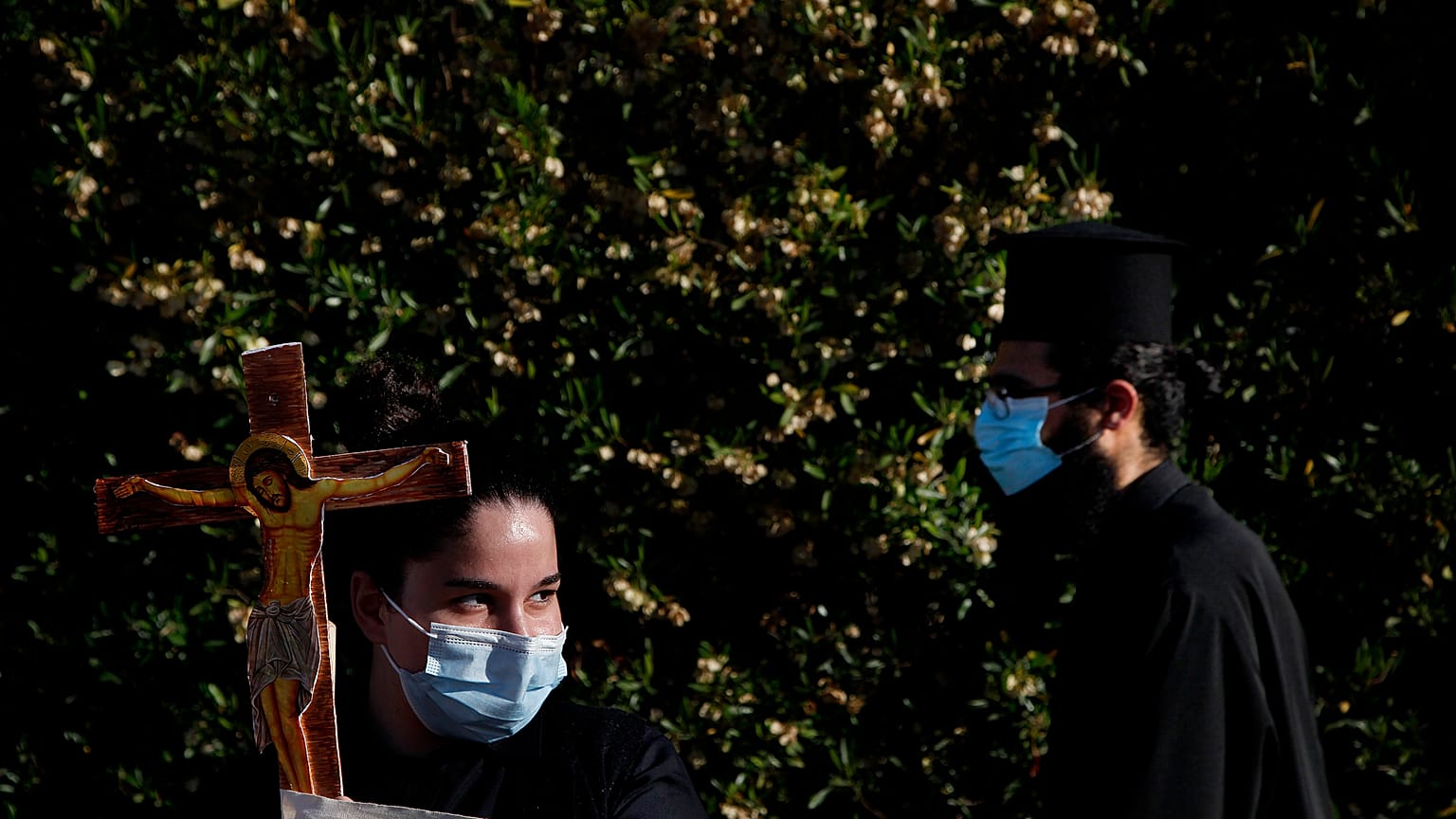A female protestor holds a cross as an Orthodox priest passes during a protest against the Cyprus' song in Eurovision.
