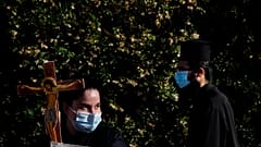 A female protestor holds a cross as an Orthodox priest passes during a protest against the Cyprus' song in Eurovision.