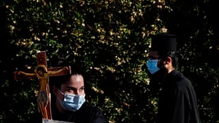 A female protestor holds a cross as an Orthodox priest passes during a protest against the Cyprus' song in Eurovision.