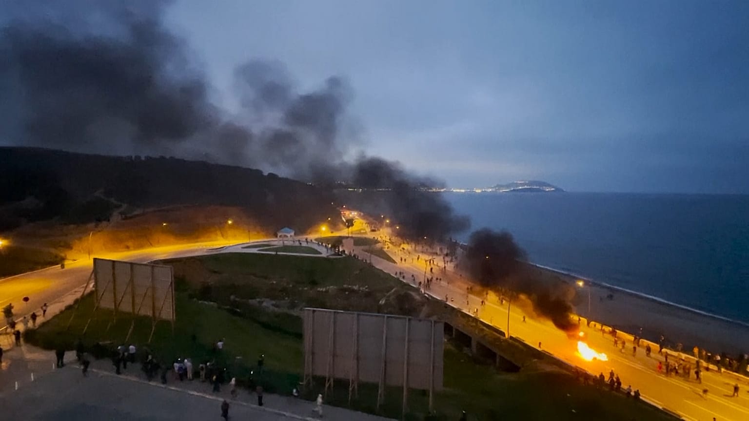 Smoke rising from burning barricade and people running.