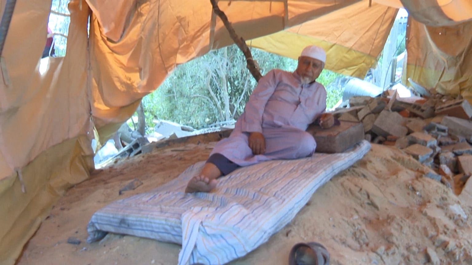 Nazmi Al-Dahdouh sitting in his tent set up over the rubble of his destroyed house
