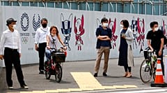 People stand by posters to promote the Tokyo Olympic Games scheduled to start in the summer of 2021, in Tokyo, Monday, May 24, 2021.
