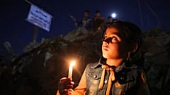 طفل فلسطيني يحمل شمعة خلال مسيرة وسط أنقاض المنازل التي دمرتها الغارات الإسرائيلية في مدينة غزة في 24 مايو 2021.