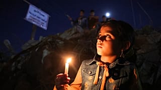 طفل فلسطيني يحمل شمعة خلال مسيرة وسط أنقاض المنازل التي دمرتها الغارات الإسرائيلية في مدينة غزة في 24 مايو 2021.
