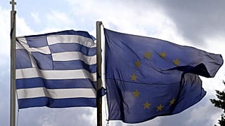 Οι σημαίες της Ελλάδας και της Ευρωπαϊκής Ένωσης ανεμίζουν με φόντο τον αττικό ουρανό.