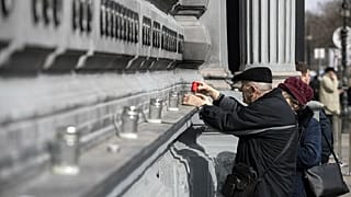 Anziani accendono candele al muro degli eroi fuori dal museo della Casa del Terrore, a Budapest, in occasione del giorno della memoria delle vittime del comunismo