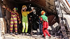 فلسطينيون يرتدون زي المهرجين يستمتعون بالأطفال وسط أنقاض مبنى دمر خلال القصف الإسرائيلي الأخير في رفح ، جنوب قطاع غزة