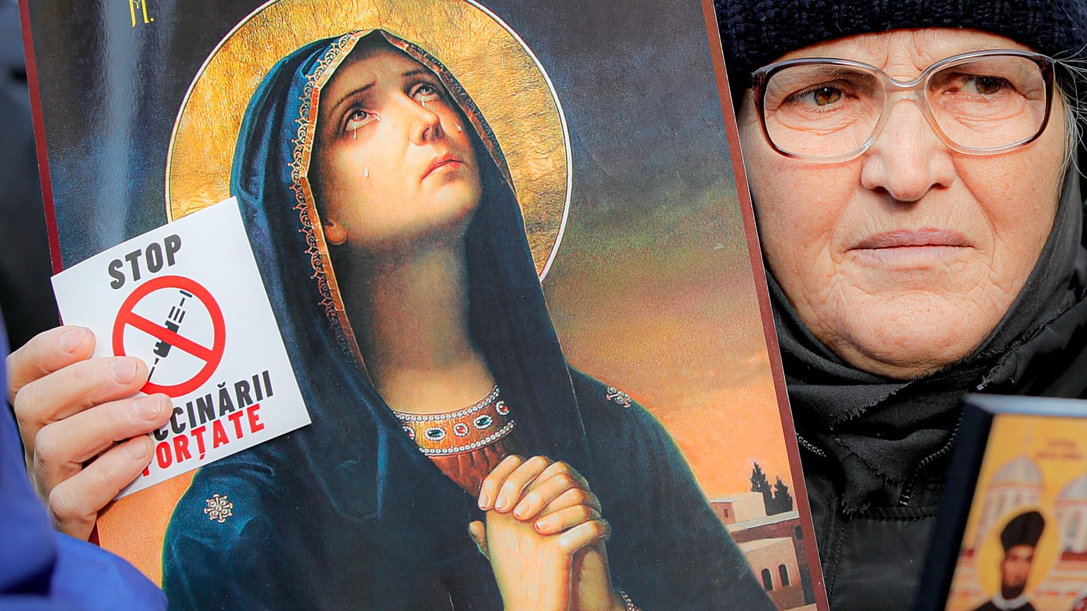 An anti-vaccination protester holds a sticker that reads "Stop the Mandatory Vaccination" next to an icon during a rally in Bucharest, Romania, Saturday, March 20, 2021. 