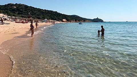 In this June 29, 2019 photo, people enjoy the white sand and crystal-clear waters of Chia Beach, on the Italian island of Sardinia.