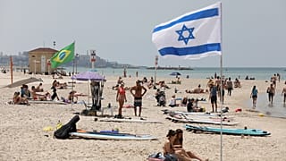 Tavaly májusi fotó: emberek napoznak és sétálnak egy tengerparti strandon Tel-Avivban