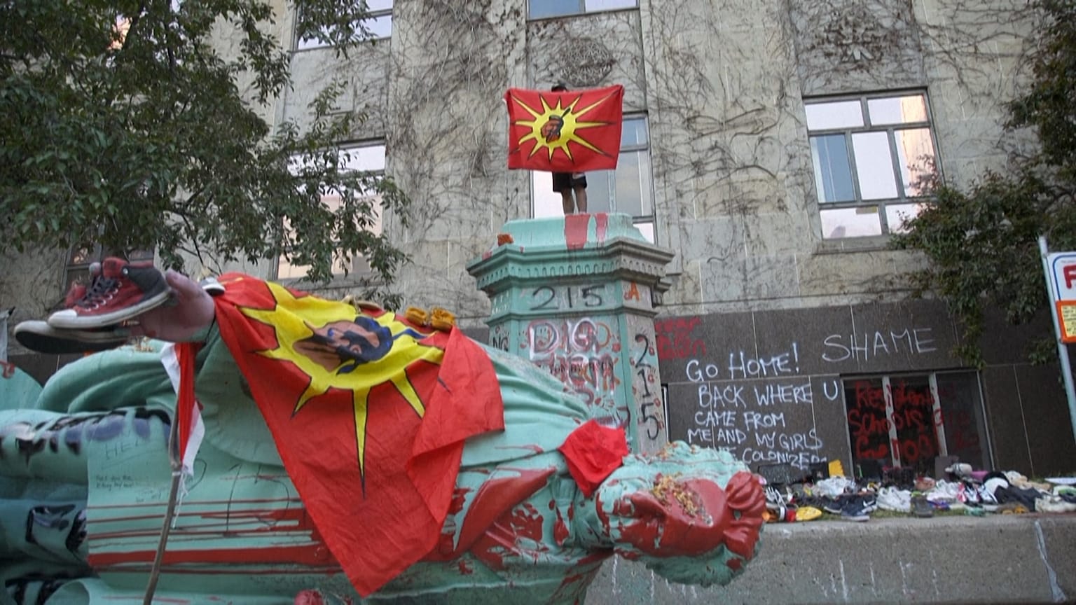 Somebody with a Mohawk flag on the pedestal where the statue of Egerton Ryerson stood, now lying on the ground.