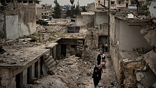 Suriye'nin İdlib kentinde, yoğun bombardıman sonucu harabeye dönen bir mahalleden geçen kadınlar (arşiv) 