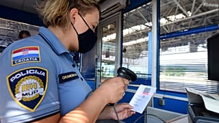 Horvát határőr szkenneli a Covid-igazolvány kódját a horvát-szlovén határon