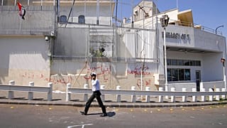 Un policía camina frente a la embajada estadounidense dañada después de que manifestantes progubernamentales atacaran la embajada en Damasco