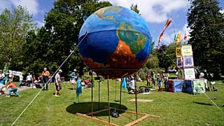 People gather around a giant globe during a climate demonstration at Kimberley Park in Falmouth, Cornwall, England, Saturday, June 12, 2021.
