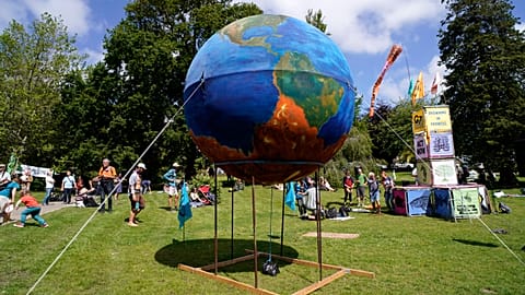 People gather around a giant globe during a climate demonstration at Kimberley Park in Falmouth, Cornwall, England, Saturday, June 12, 2021.