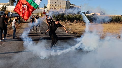 A Palestinian demonstrator returns a tear gas canister fired by Israeli forces.