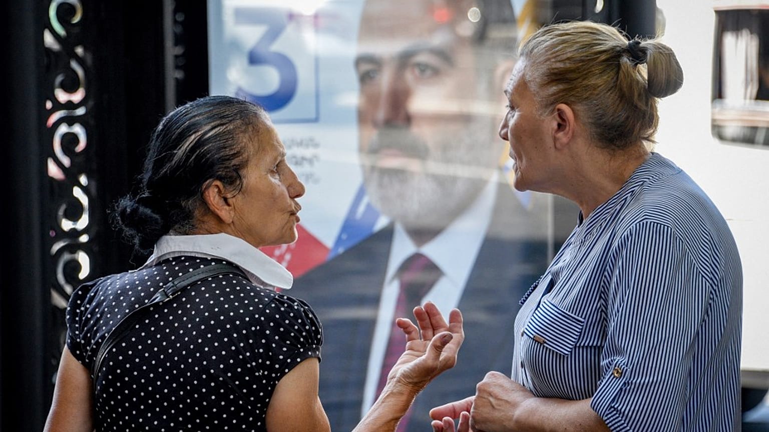 Deux femmes échangent à Erevan, devant une affiche de campagne, le 16 juin 2021, Arménie