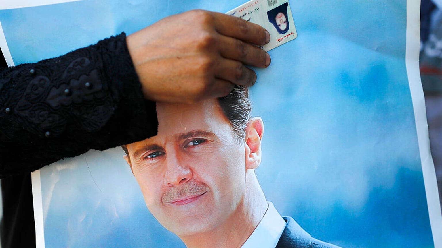 maggio 2020: una profuga siriana in Libano tiene in vista la sua carta d'identità su un poster di Basar al-Assad
