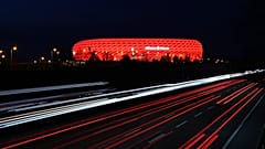 FILE - In this Monday, March 16, 2020 file photo, cars pass the illuminated 'Allianz Arena' soccer stadium in Munich, Germany. 