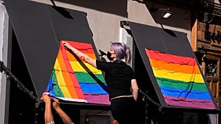 A woman hangs rainbow flags on the outside of a restaurant on the first day of the annual LGBT+ pride week in Madrid.
