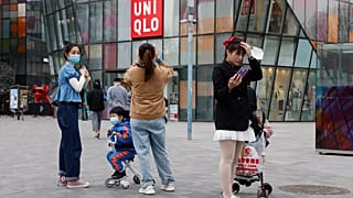 In this Monday, March 29, 2021 file photo, visitors to a shopping mall wearing masks stand before a Uniqlo store in Beijing.